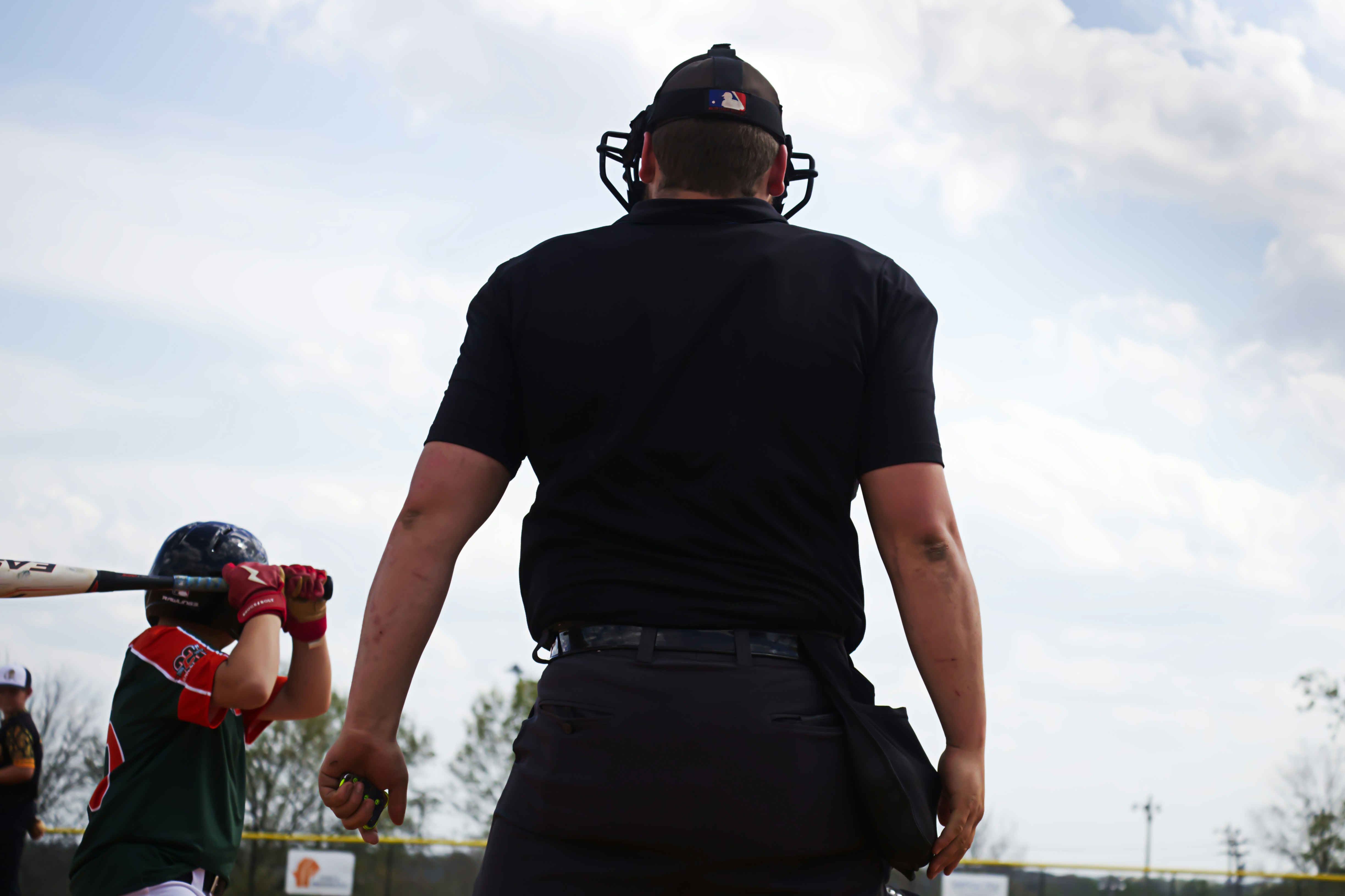 Baseball umpire in black uniform faces young batter in red during youth baseball game