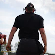 Baseball umpire in black uniform faces young batter in red during youth baseball game