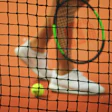 Tennis player's leg and racket on orange clay court viewed through net