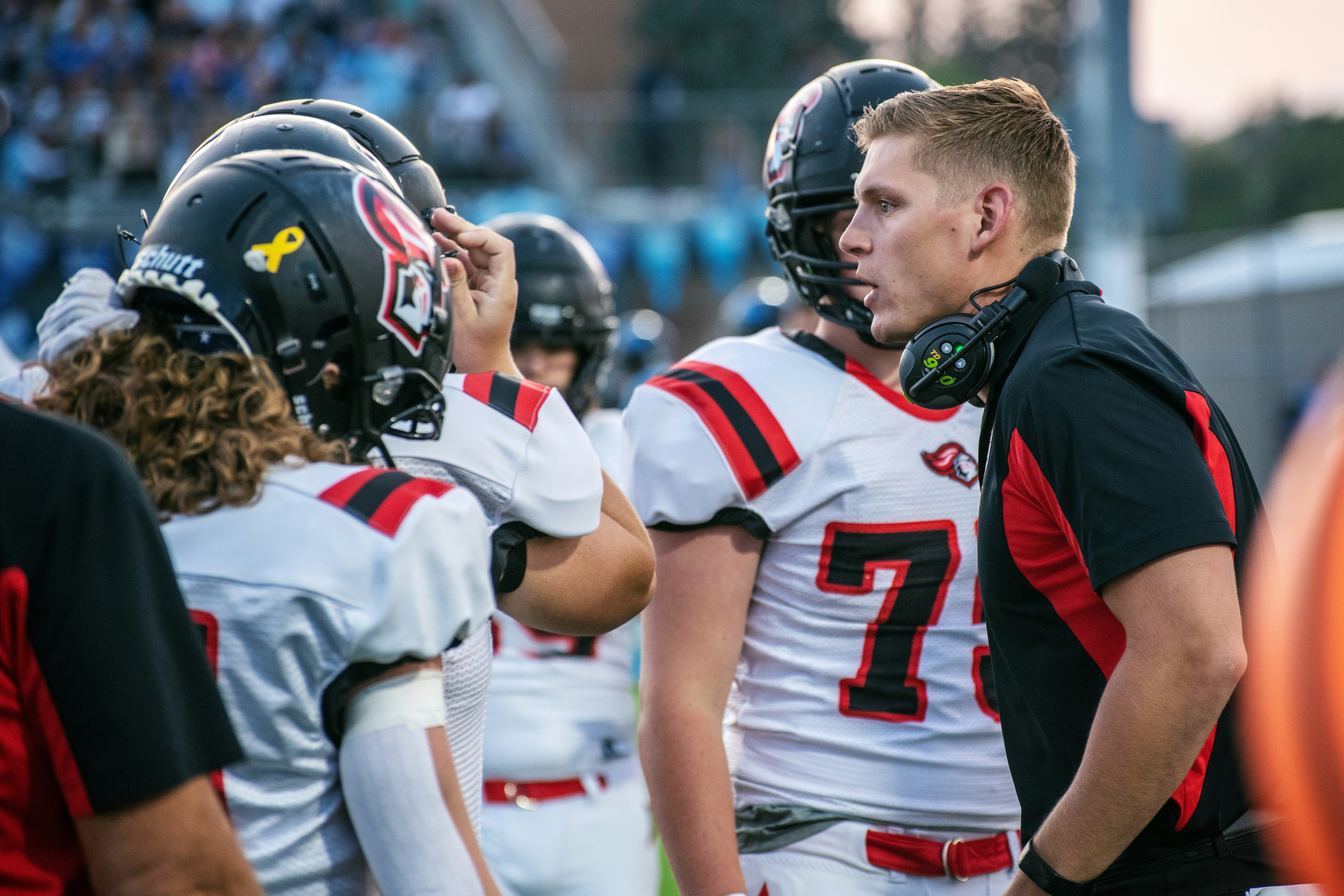Football coach in headset speaks with players wearing red and white uniforms during game