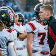 Football coach in headset speaks with players wearing red and white uniforms during game