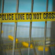 Yellow and black police caution tape reading 'POLICE LINE DO NOT CROSS' stretched across a metal fence