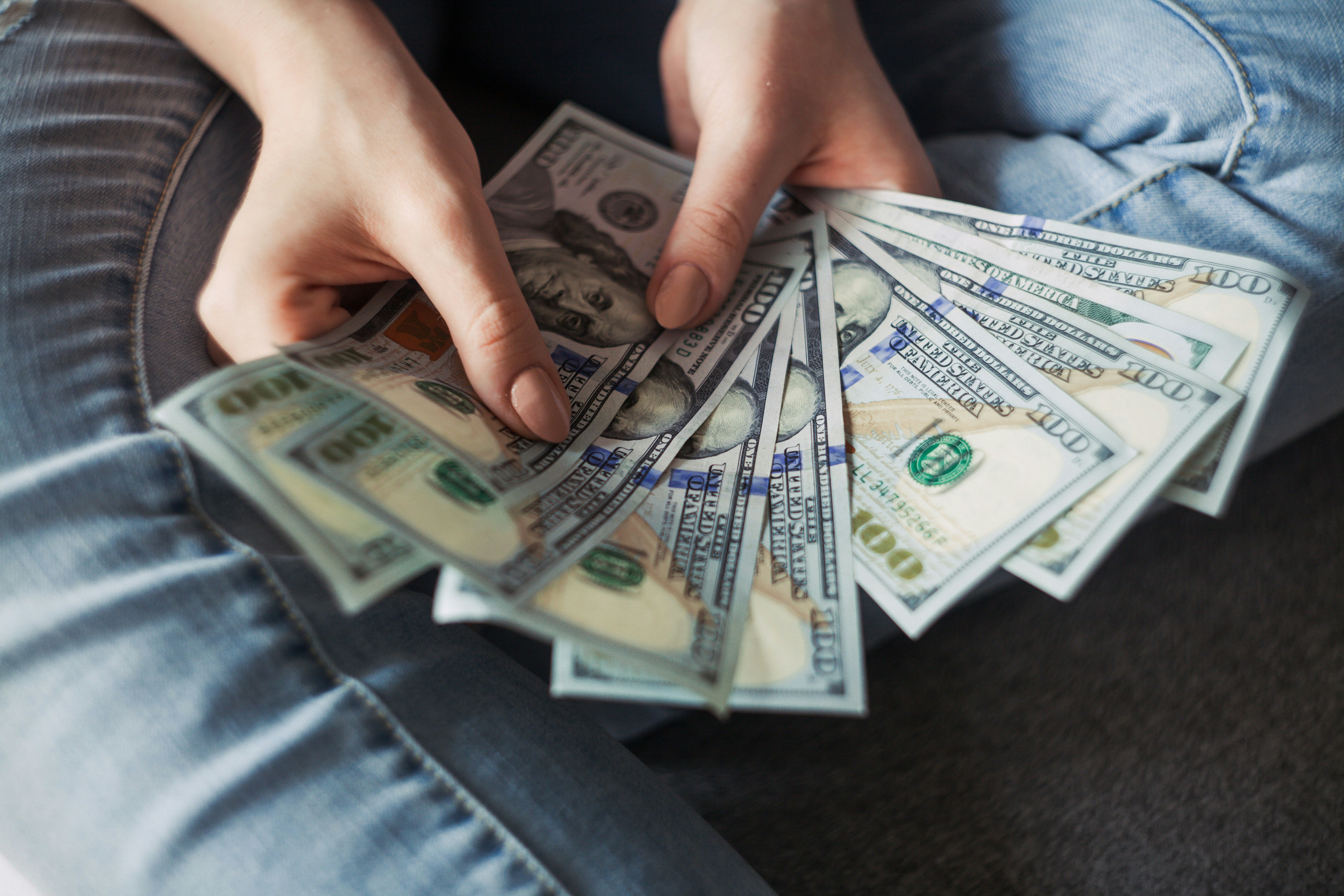 Hands holding and counting multiple US dollar bills in a fan arrangement