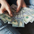 Hands holding and counting multiple US dollar bills in a fan arrangement