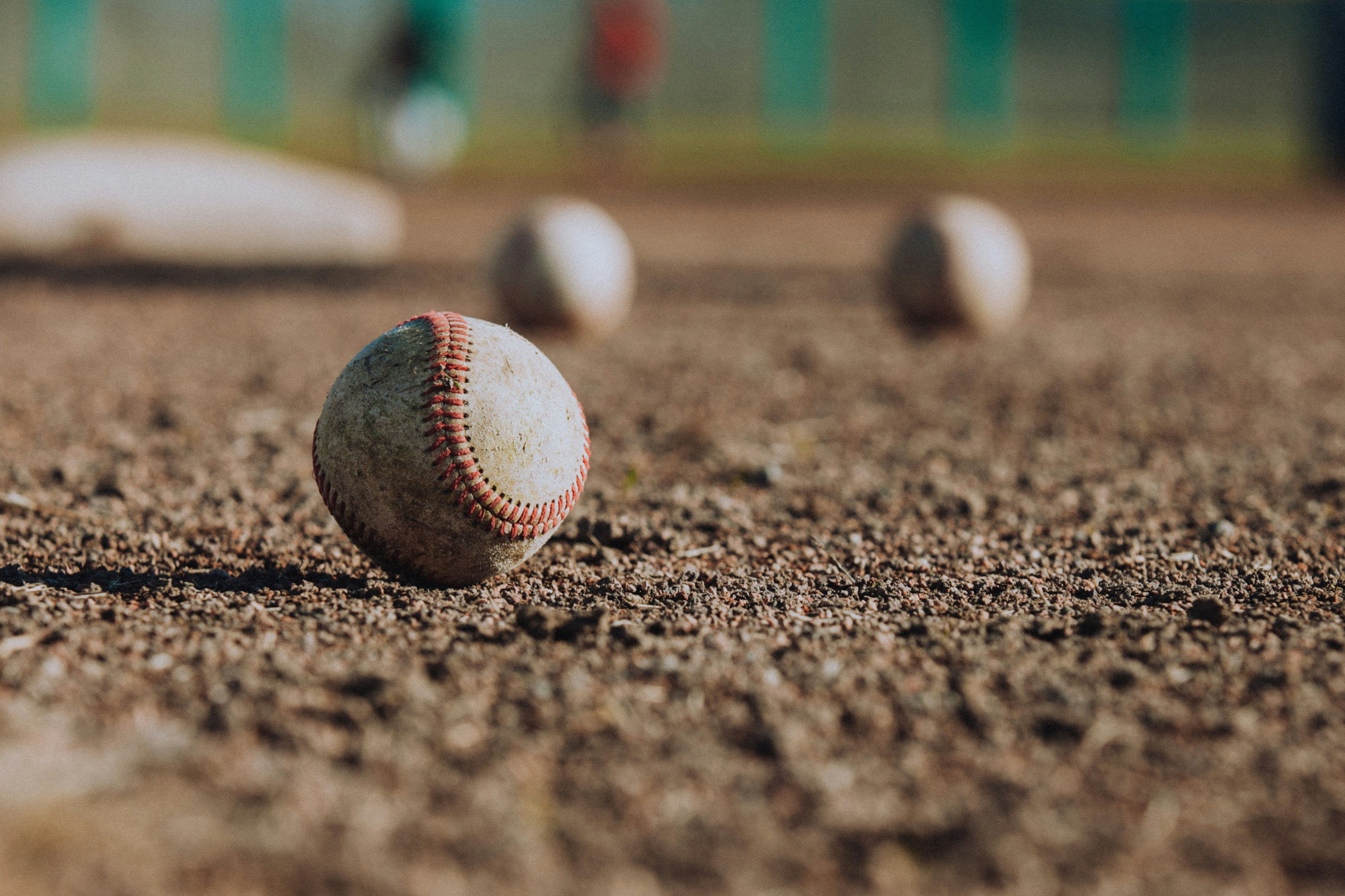 Worn baseball resting on infield dirt with additional baseballs visible in background