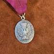 Silver medallion award with eagle emblem and purple ribbon on cork background