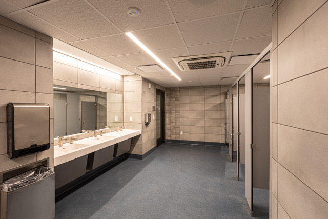 A community recreation center restroom with the following hygiene attributes: scrubbable ceiling tile, monolithic epoxy floor with integral cove base, touchless fixtures and accessories, and anti-microbial hardware.