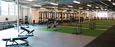 Modern fitness facility with strength training equipment, cardio machines, artificial turf, and functional training areas