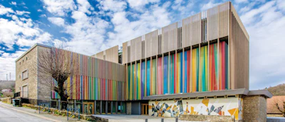 Modern institutional building with colorful vertical striped facade and stone base under blue sky