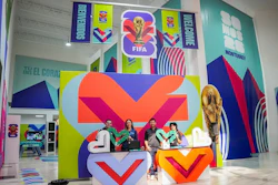 FIFA World Cup 2022 exhibition space with colorful geometric branding, large V-shaped logo installation, and visitors at interactive display area