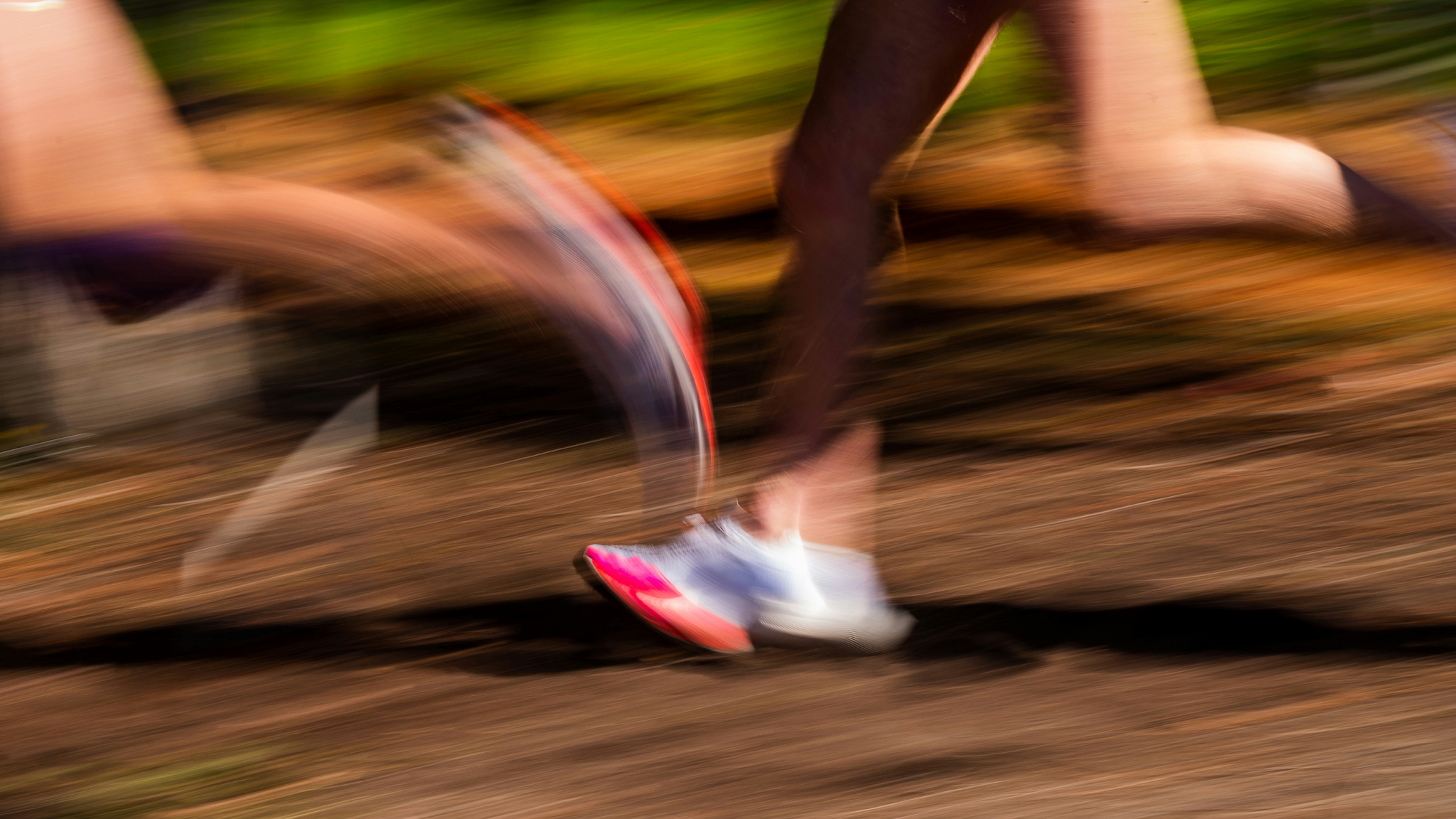 Runner sprinting on a dirt trail with motion blur, wearing pink and white athletic shoes