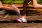 Runner sprinting on a dirt trail with motion blur, wearing pink and white athletic shoes