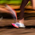 Runner sprinting on a dirt trail with motion blur, wearing pink and white athletic shoes