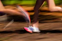Runner sprinting on a dirt trail with motion blur, wearing pink and white athletic shoes