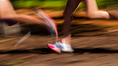 Runner sprinting on a dirt trail with motion blur, wearing pink and white athletic shoes