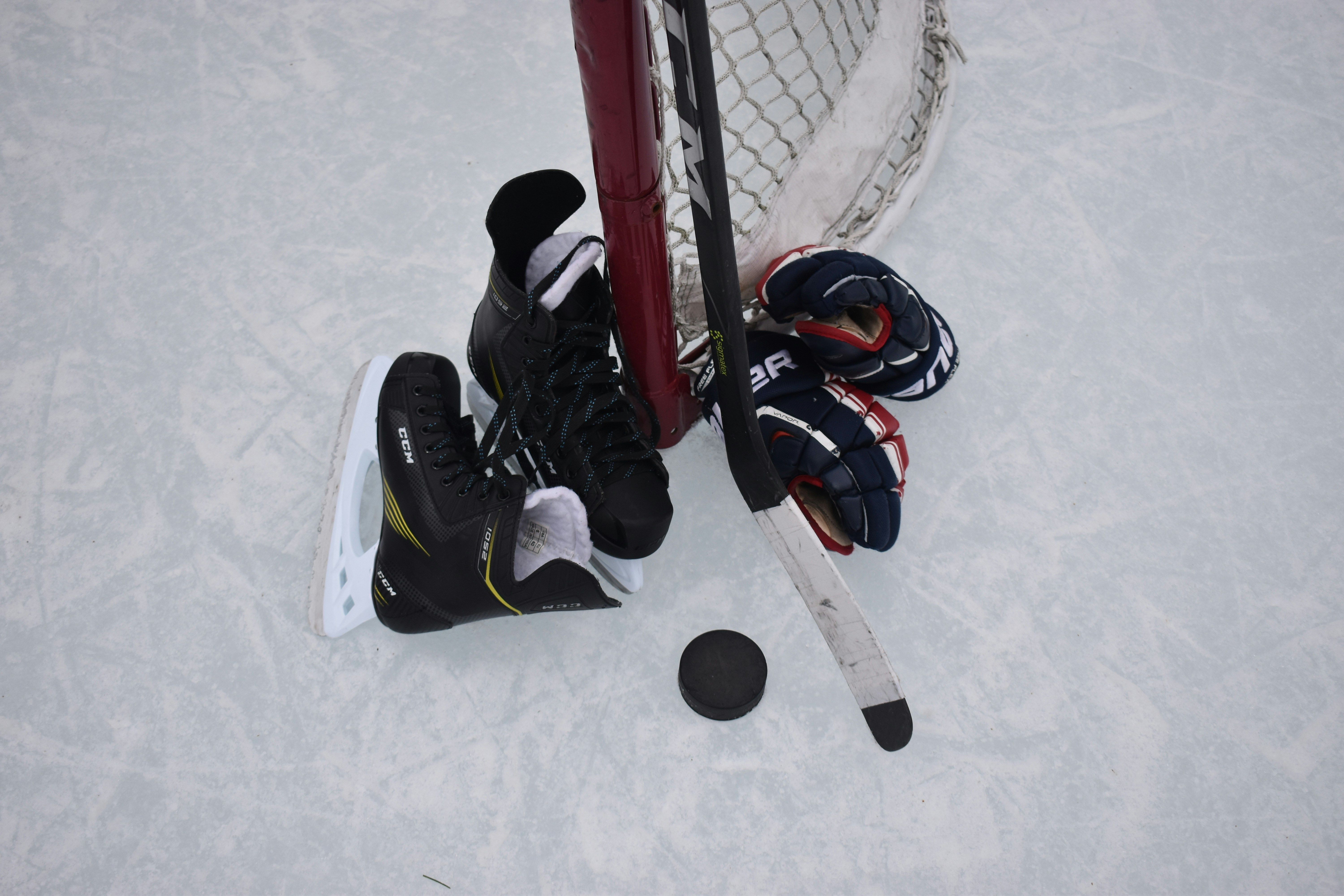 Overhead view of ice hockey players competing near the goal net with stick and puck on ice