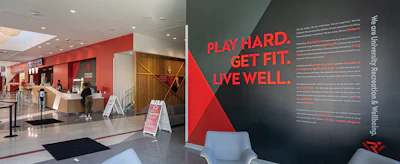 Modern fitness facility entrance with red and black branded wall featuring 'Play Hard. Get Fit. Live Well.' motivational text and mission statement.