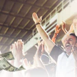 Excited group of people celebrating with arms raised as money falls around them in a bright, successful moment