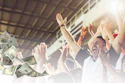 Excited group of people celebrating with arms raised as money falls around them in a bright, successful moment