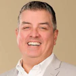 Professional headshot of a smiling man in business casual attire against a neutral background