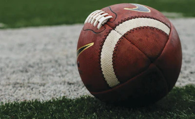 Brown football with white laces and cream stripe on grass field