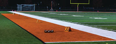 Baseball field with orange infield dirt, white foul lines, and yard markers during evening practice setup.