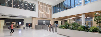 Modern building lobby with double-height atrium, reception desk, green plants, and natural lighting from large windows