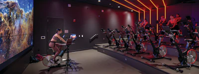 Group fitness class with cyclists on stationary bikes in a modern studio with neon orange lighting