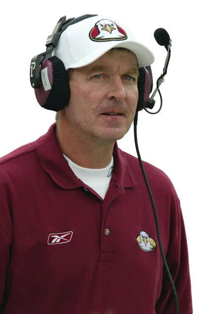Football coach wearing maroon polo shirt and white cap with headset during game