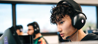 Young gamer wearing black headphones with microphone in esports facility with teammates in background