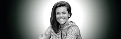 Professional headshot of smiling woman with dark hair wearing striped shirt against neutral background
