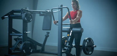 Woman in red tank top using leg press machine in modern gym with blue lighting