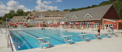 Outdoor Olympic-style swimming complex with multiple lap pools, diving boards, and red brick facility buildings surrounded by landscaping.