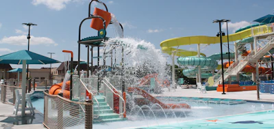Busy water park with bucket dumping water feature, slides, and pools on a sunny day