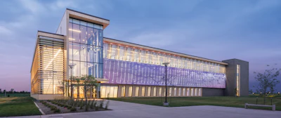 Modern glass and steel institutional building illuminated at twilight with manicured lawn and pathway