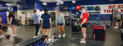 Group fitness class at gym with people exercising near equipment and motivational wall signage