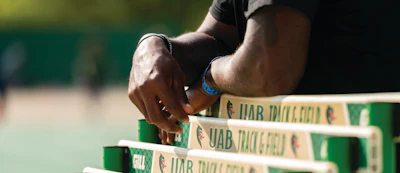 Athlete's hand touching green branded hurdles during track and field training or competition