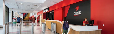Modern reception lobby with red and black accent walls, wooden reception desk, and Recreation & Wellbeing signage