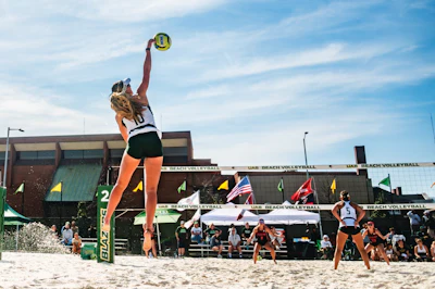 Female beach volleyball player jumping to spike ball during UAB tournament match on sandy court