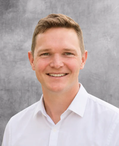 Professional headshot of a smiling man in a white collared shirt against a gray background