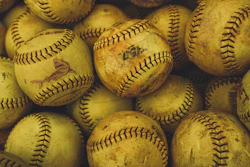 Collection of worn yellow softballs with black stitching and manufacturer markings