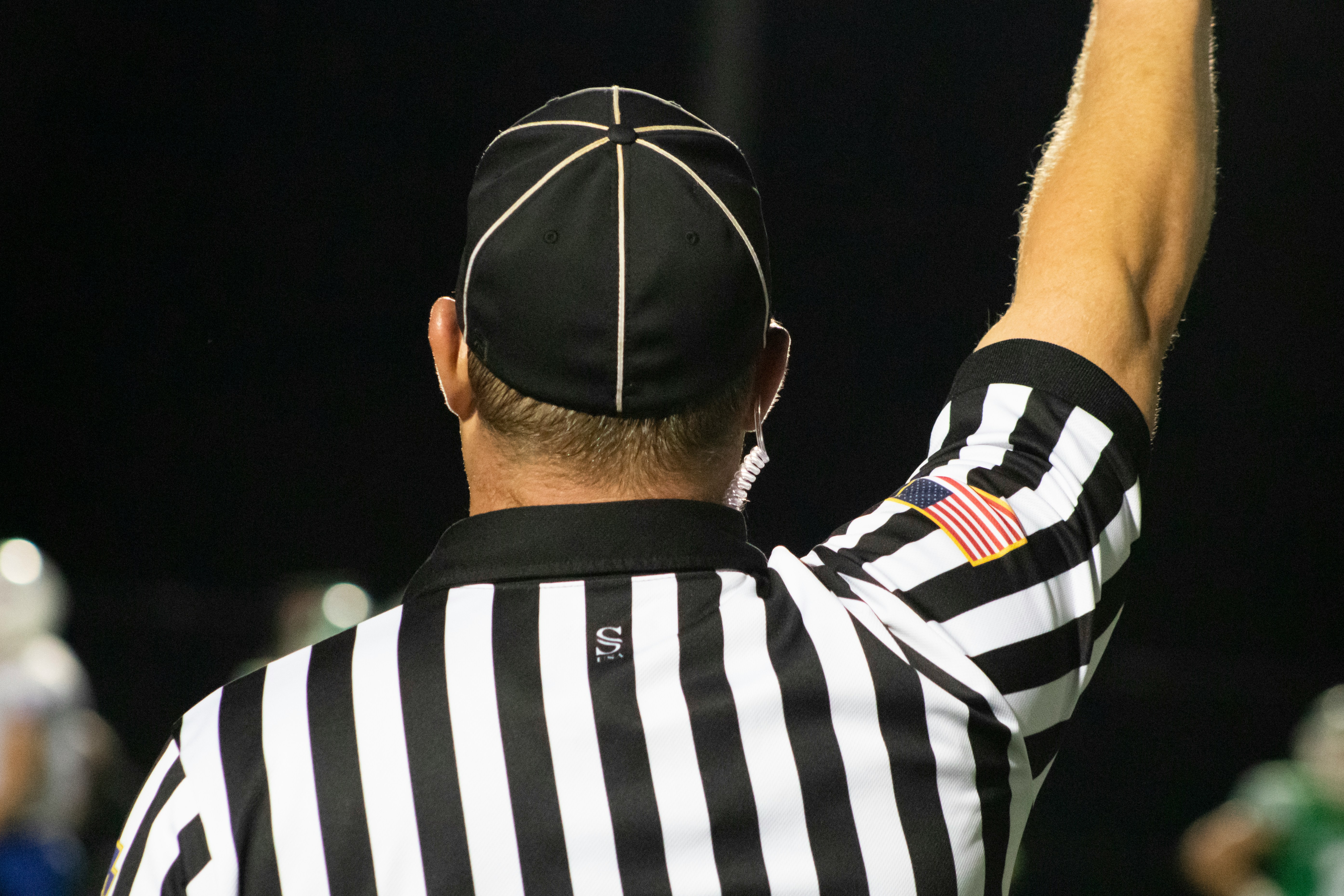Sports referee in black and white striped uniform raising arm during game with American flag patch visible