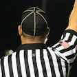 Sports referee in black and white striped uniform raising arm during game with American flag patch visible