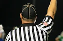 Sports referee in black and white striped uniform raising arm during game with American flag patch visible
