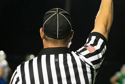 Sports referee in black and white striped uniform raising arm during game with American flag patch visible