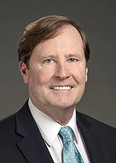Professional headshot of a smiling man in business attire with teal patterned tie