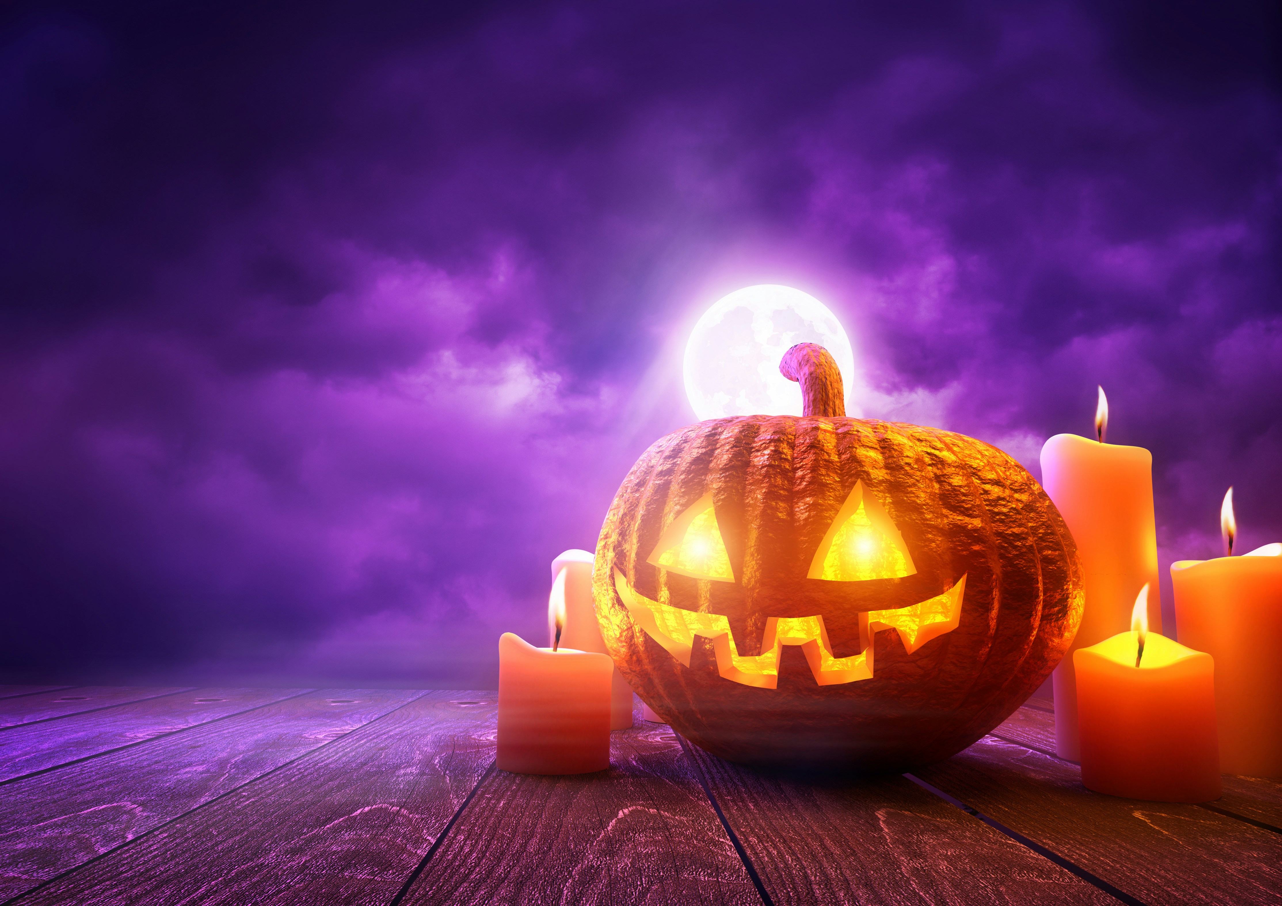Glowing jack-o'-lantern surrounded by lit candles against a purple moonlit sky on wooden surface
