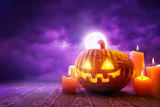 Glowing jack-o'-lantern surrounded by lit candles against a purple moonlit sky on wooden surface