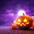 Glowing jack-o'-lantern surrounded by lit candles against a purple moonlit sky on wooden surface