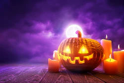 Glowing jack-o'-lantern surrounded by lit candles against a purple moonlit sky on wooden surface